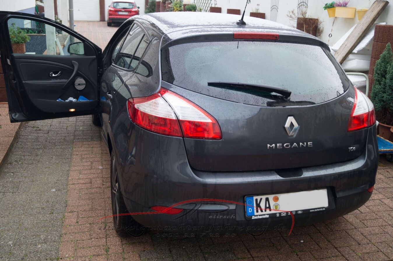 Ein dunkelgrauer Renault Megane steht auf einem gepflasterten Platz mit geöffneter Fahrertür.