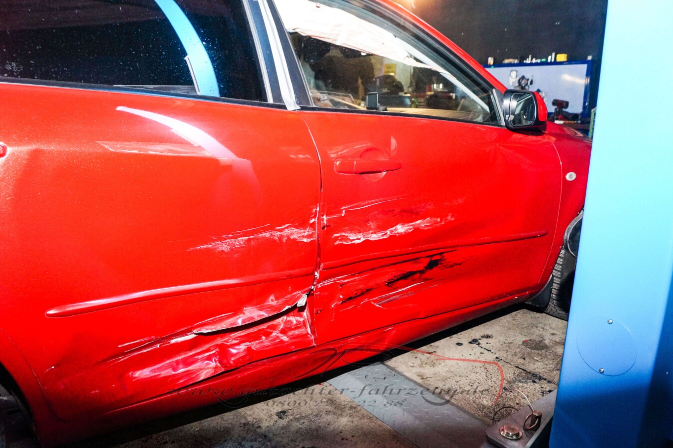 Ein rotes Auto mit einer sichtbaren Kratzer- und Schadenstelle an der Fahrertür.
