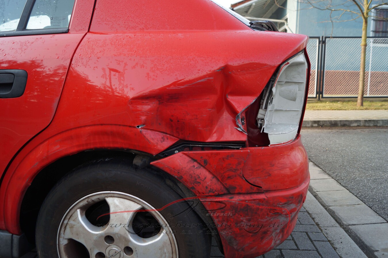 Ein rotes Auto mit einem starken Schaden am Heck, der die Stoßstange und den Kotflügel beschädigt hat.