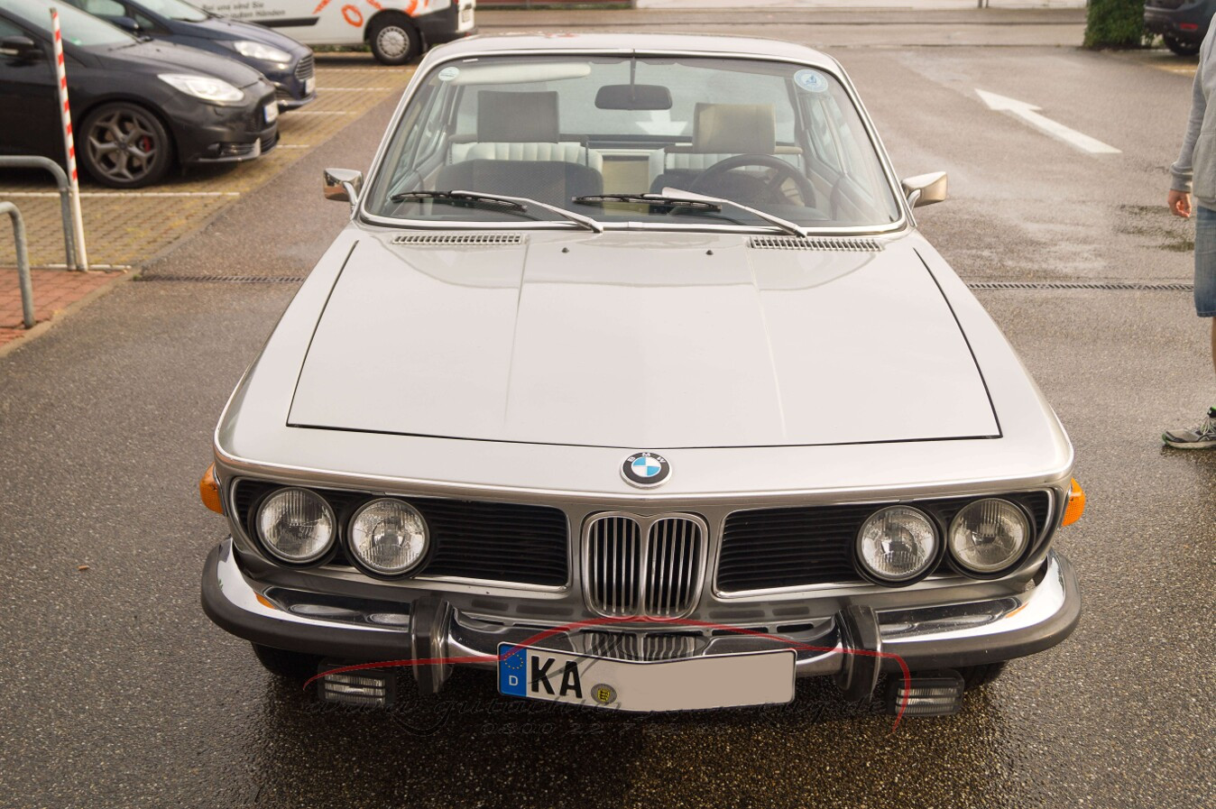 Ein silbernes BMW-Coupé mit vier Scheinwerfern steht auf einem Parkplatz.