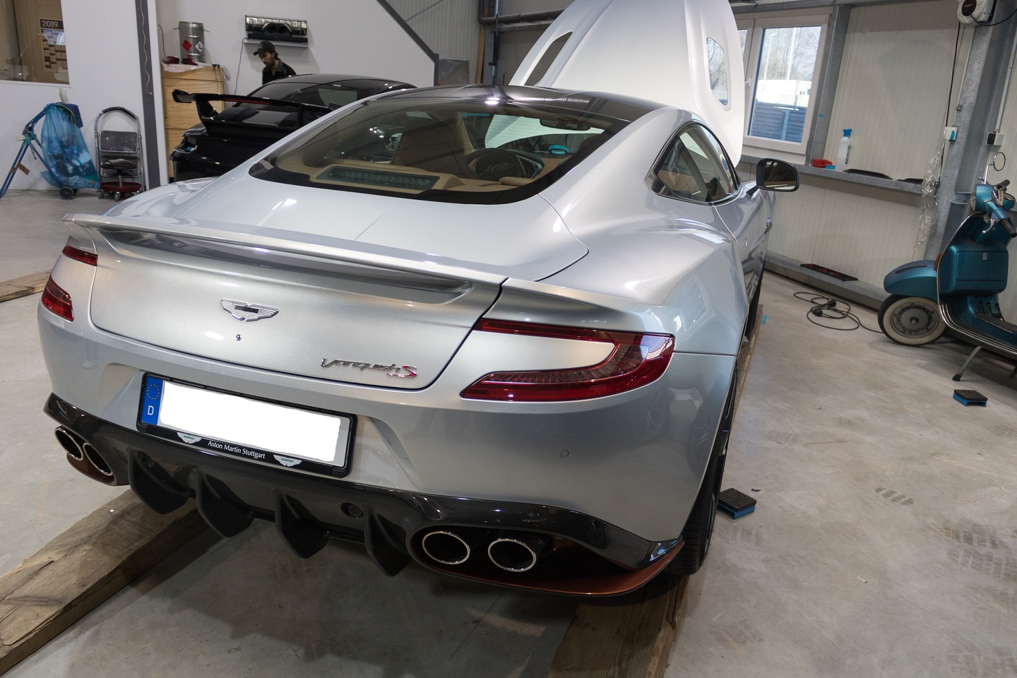 Rückansicht eines silbernen Aston Martin Vantage S in einer Werkstatt.