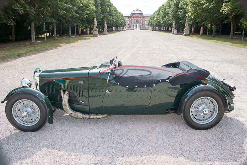 Ein grünes Vintage-Automobil steht auf einer Allee vor einem klassischen Schloss mit Säulen und Skulpturen.