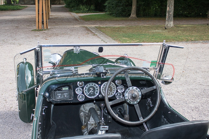 Innenraum eines grünen Oldtimers mit Lenkrad, Armaturenbrett und offener Karosserie.