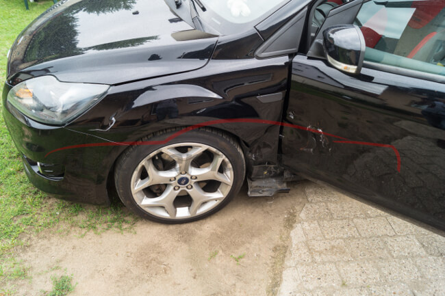 Ein schwarzes Auto mit einem sichtbaren Schaden an der vorderen Fahrertür und dem Kotflügel.