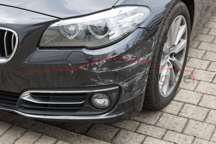 Nahaufnahme des vorderen Kotflügels und Scheinwerfers eines dunklen BMW-Autos auf gepflastertem Boden.