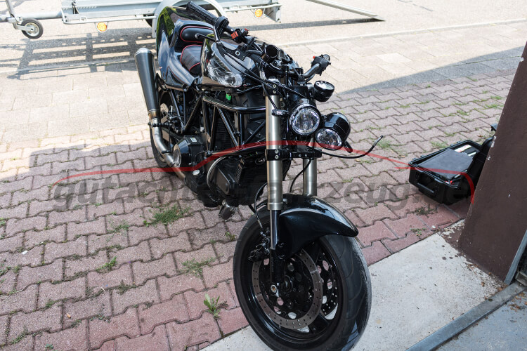 Ein schwarzes Motorrad mit auffälligen Scheinwerfern steht auf einem gepflasterten Platz.