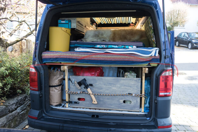 Der geöffnete Kofferraum eines Autos ist mit Werkzeugen, einem Bett und anderen Gegenständen vollgestellt.