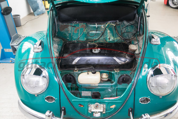 Ein grünes Klassik-Auto mit geöffneter Motorhaube zeigt den darunterliegenden Motorraum.